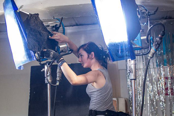 A Gaffer operating a lamp with color correction gels on set of a video production.
