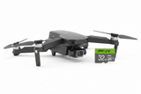 A black DJI drone with its propellers extended, shown next to a green and black PNY Elite 32GB microSD card on a clean white background.